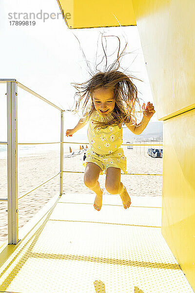 Fröhliches Mädchen springt auf gelbe Rettungsschwimmerhütte
