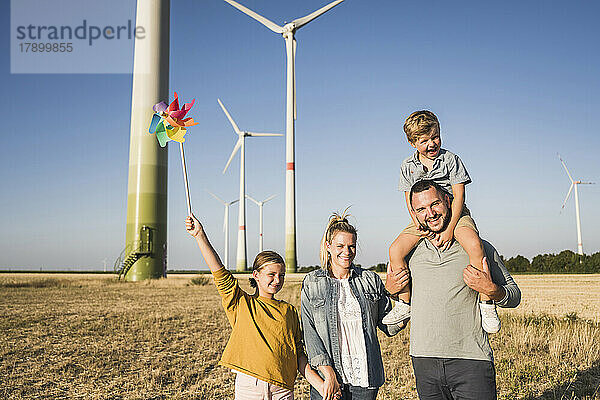 Optimistische Familie geht im Windpark spazieren. Tochter trägt buntes Windrad