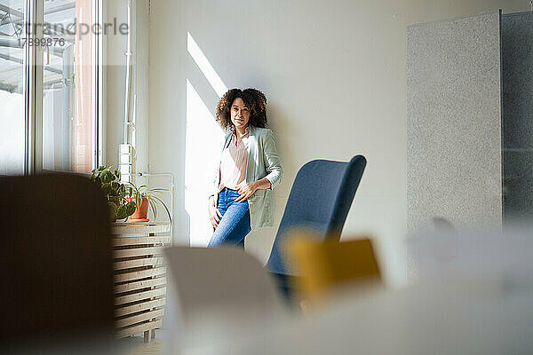 Confident businesswoman leaning on wall at office