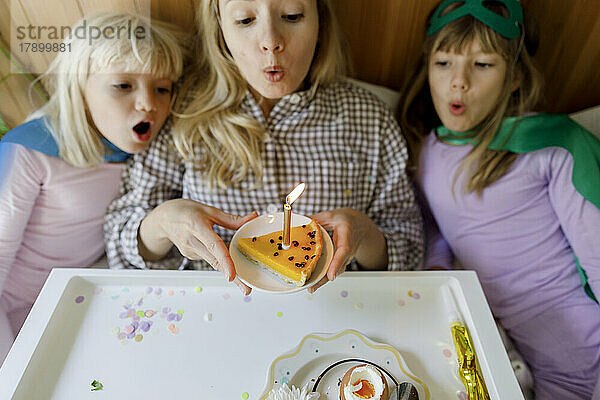 Mutter mit Kindern bläst zu Hause Kerze auf Kuchen
