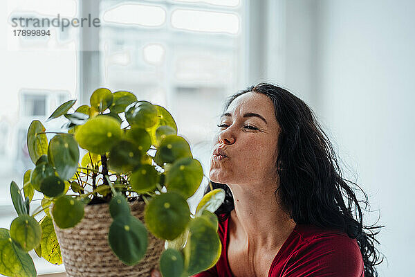 Frau küsst Zimmerpflanze am Fenster