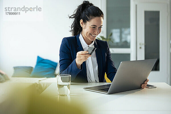 Glückliche Geschäftsfrau mit Kreditkarte beim Online-Einkauf per Laptop