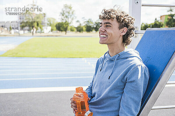 Glücklicher Sportler hält an einem sonnigen Tag eine Wasserflasche in der Hand