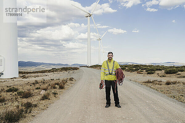 Ingenieur mit Helm und Seil steht auf der Straße am Windpark