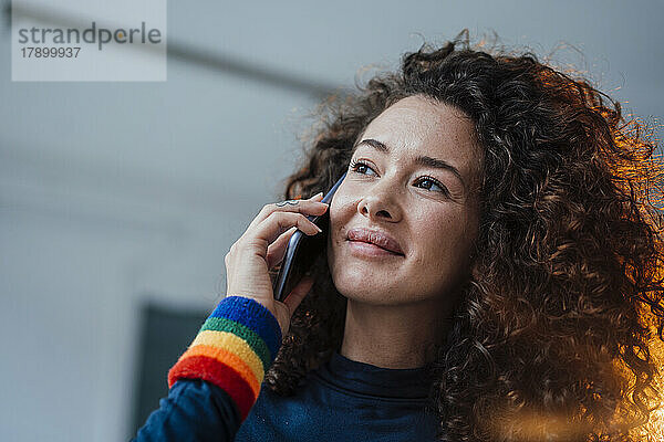 Lächelnde schöne junge Frau mit Regenbogenarmband  die mit dem Handy spricht