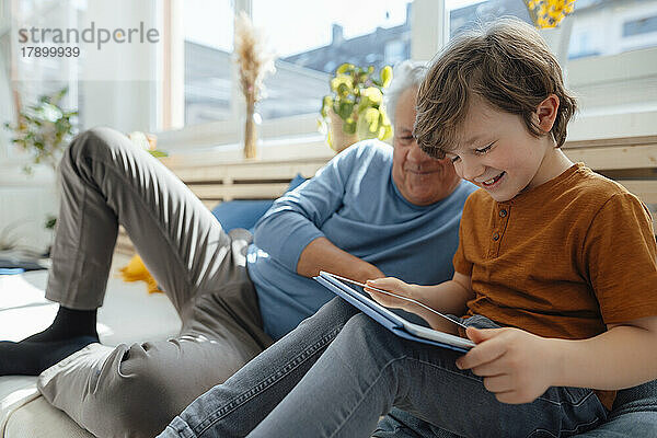Glücklicher Enkel nutzt Tablet-PC von Großvater im Wohnzimmer