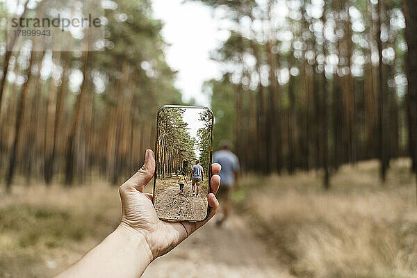 Frau mit Smartphone fotografiert Mann und Mädchen beim Spaziergang im Wald