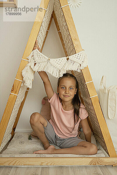 Smiling cute girl with hand raised sitting in tent at home