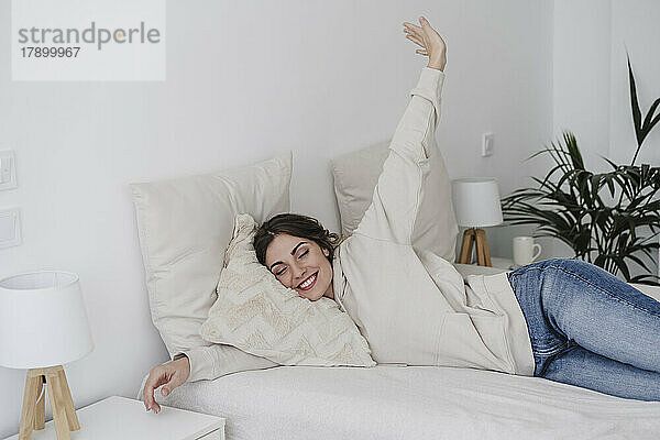 Lächelnde junge Frau entspannt sich zu Hause im Bett