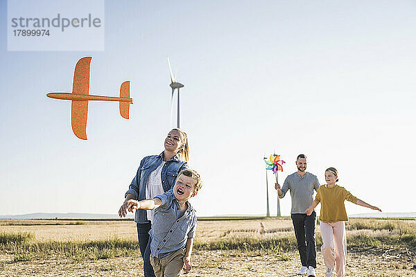 Glückliche Familie  die durch den Windpark spaziert. Kinder tragen Spielzeug