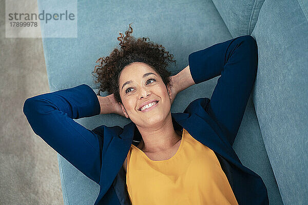 Smiling businesswoman with hands behind head lying on sofa