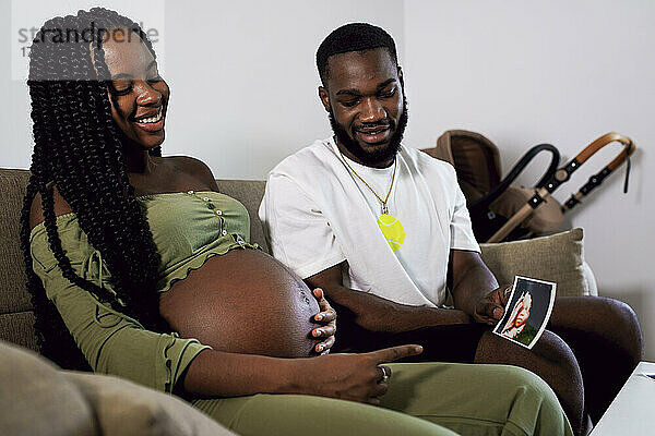 Mann zeigt schwangerer Frau zu Hause Ultraschallbild des Babys