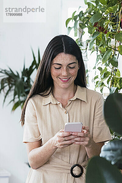 Lächelnde junge Geschäftsfrau  die im Büro Textnachrichten über das Smartphone sendet