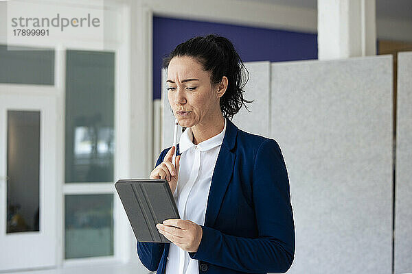 Nachdenkliche Geschäftsfrau mit digitalisiertem Stift und Blick auf den Tablet-PC