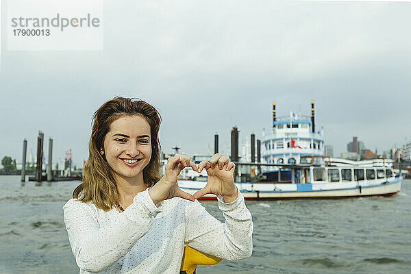 Lächelnde Frau gestikuliert Herzform im Hamburger Hafen  Deutschland