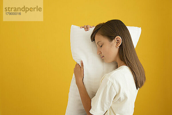 Girl with eyes closed resting her face on pillow against yellow background