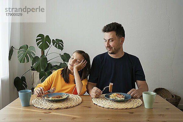 Müdes Mädchen mit Vater beim Frühstück am Esstisch