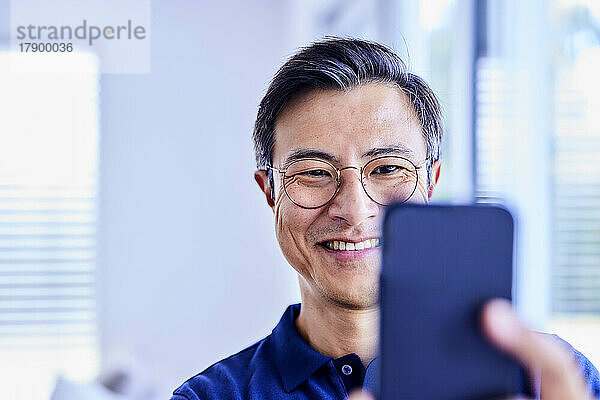 Happy mature man taking selfie through smart phone at home