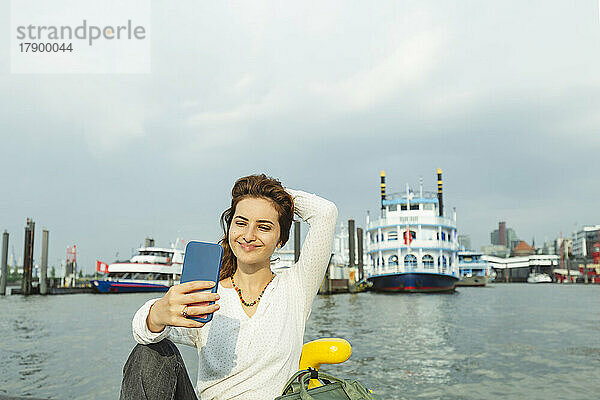 Lächelnde Frau macht ein Selfie mit ihrem Smartphone im Hamburger Hafen