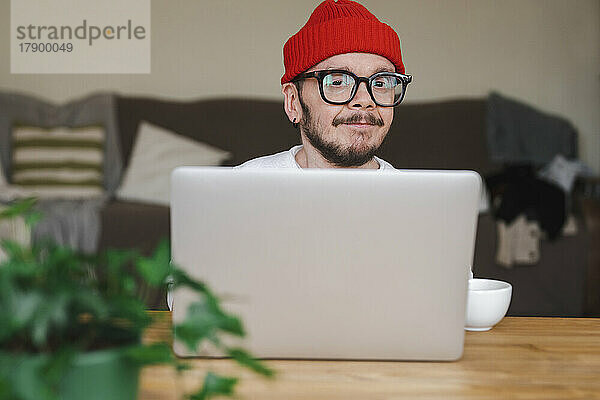 Mann mit Brille sitzt zu Hause vor Laptop