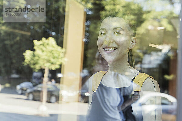 Lächelnde nicht-binäre Person durch Glas gesehen