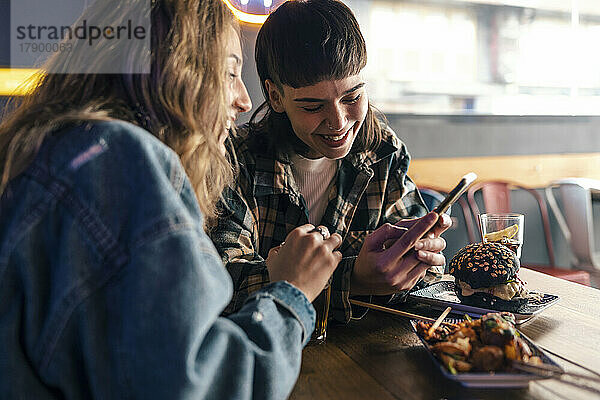 Glückliches lesbisches Paar benutzt Smartphone am Tisch im Restaurant