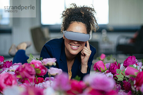 Lächelnde Geschäftsfrau mit VR-Brille neben Blumen im Büro