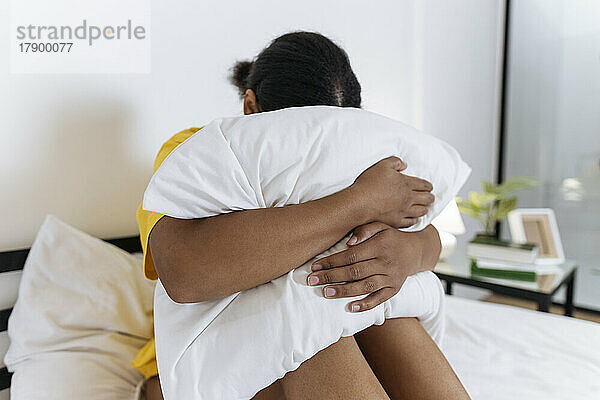 Verärgerte Frau versteckt ihr Gesicht im Kissen  während sie auf dem Bett sitzt