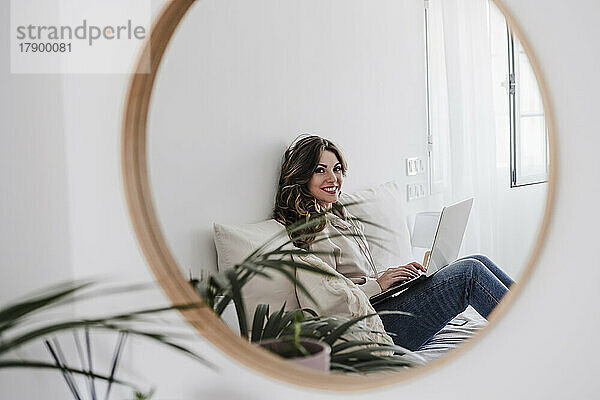 Spiegelbild einer lächelnden Frau mit Laptop im Spiegel zu Hause