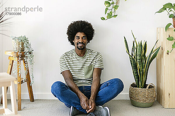 Lächelnder Mann mit Afro-Frisur sitzt vor der Wand