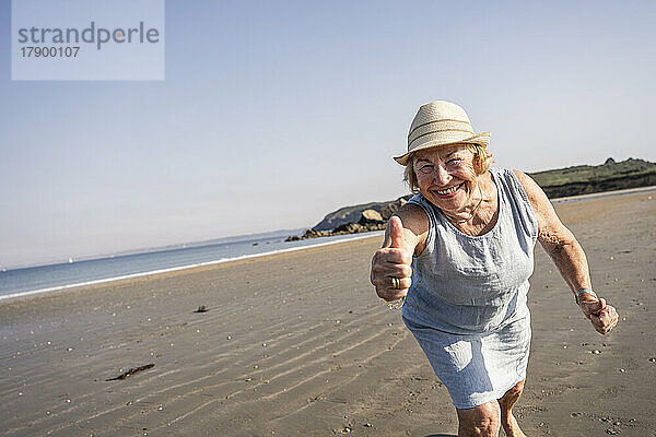 Glückliche ältere Frau zeigt Daumen nach oben am Strand