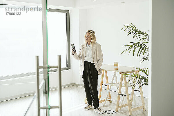 Geschäftsfrau steht im modernen Büro und benutzt Mobiltelefon