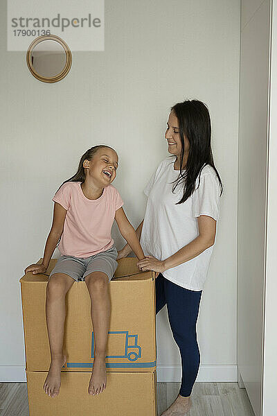 Mutter blickt glückliche Tochter an  die auf einer Kiste sitzt