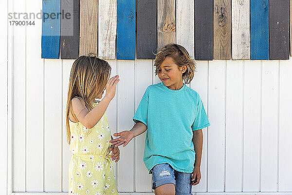Girl playing clapping game with brother in front of wooden wall