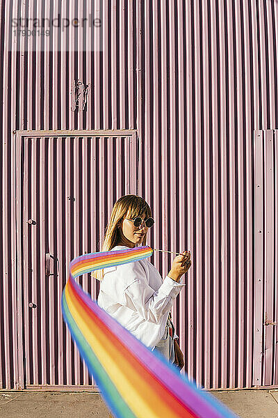 Frau hält regenbogenfarbenes Gymnastikband vor Wellwand