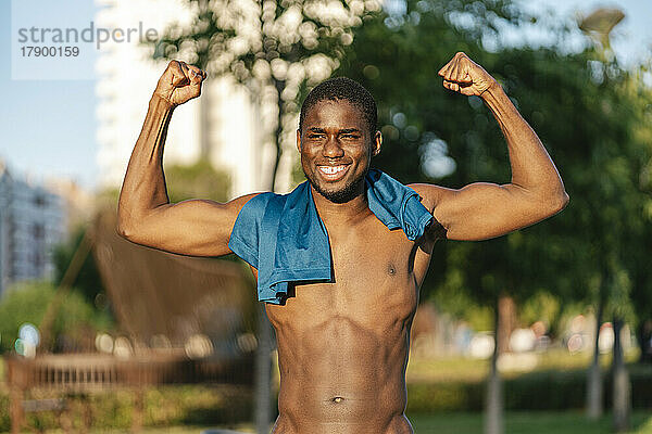 Lächelnder junger Mann  der an einem sonnigen Tag seine Muskeln spielen lässt