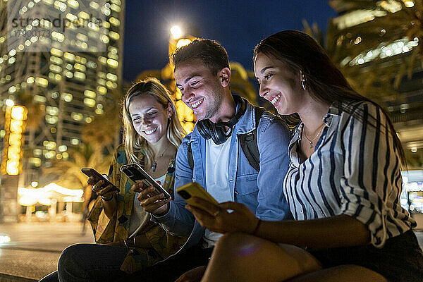 Glücklicher junger Mann  der nachts sein Smartphone mit Freunden teilt