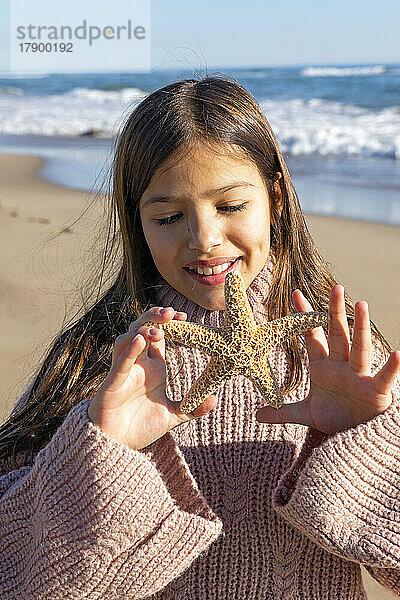 Mädchen spielt an einem sonnigen Tag mit Seesternen am Strand