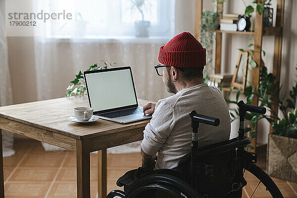 Mann im Rollstuhl benutzt Laptop zu Hause