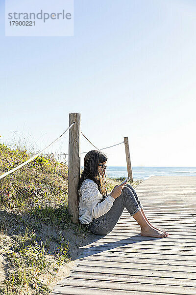 Girl reading book sitting on boardwalk at beach