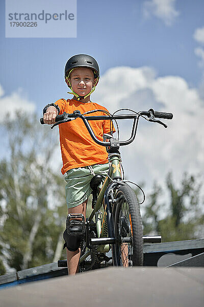 Junge sitzt auf einem BMX-Fahrrad an der Sportrampe