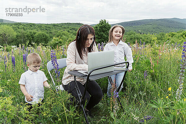 Mutter arbeitet am Laptop mit verspielten Kindern auf der Wiese