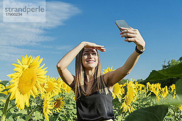 Lächelnde Frau macht Selfie per Smartphone im Sonnenblumenfeld