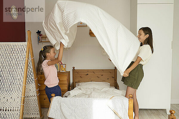 Sisters making bed in children's room at home