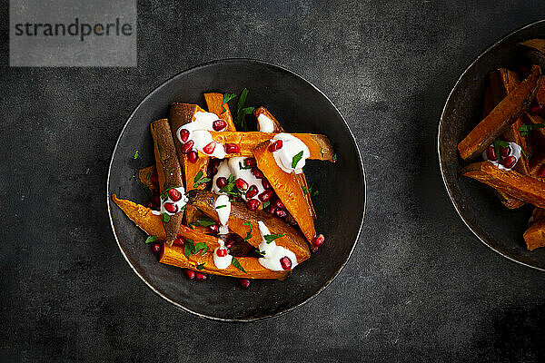 Studio shot of two bowls of sweet potatoes with parsley  pomegranate seeds and yogurt sauce