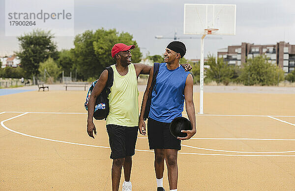 Lächelnder junger Mann hält Basketball und geht mit Vater auf dem Sportplatz spazieren