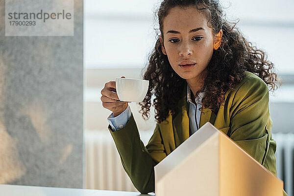 Junger Architekt mit Kaffeetasse betrachtet Musterhaus im Büro