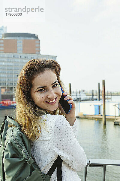 Lächelnde Frau  die am Geländer im Hamburger Hafen steht und mit ihrem Smartphone spricht