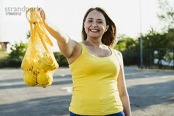 Glückliche Frau hält Netzbeutel mit Zitronen