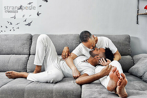 Liebevolles schwules Paar küsst sich zu Hause auf dem Sofa
